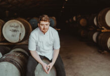A young man in chef's whites sits in a whisky store