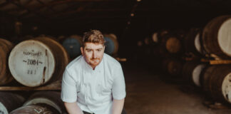 A young man in chef's whites sits in a whisky store