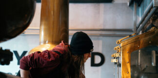 A woman in a woolly hat fiddles with the spirit safe in a distillery