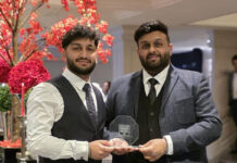 Two smartly-dressed brothers hold an award, with a pink-blossom tree behind them.