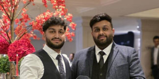 Two smartly-dressed brothers hold an award, with a pink-blossom tree behind them.