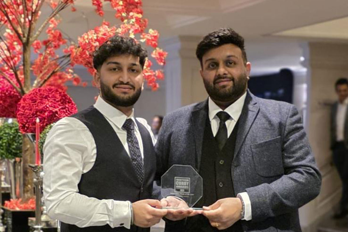 Two smartly-dressed brothers hold an award, with a pink-blossom tree behind them.