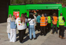 People queue at a bright green food van, in the sunshine.