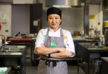 A young asian woman wearing a professional chef uniform stands in a kitchen