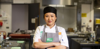 A young asian woman wearing a professional chef uniform stands in a kitchen