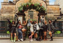 A group of young women in summer clothes celebrate at the gate of an outdoors bar