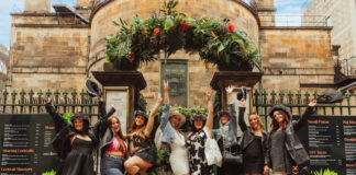 A group of young women in summer clothes celebrate at the gate of an outdoors bar