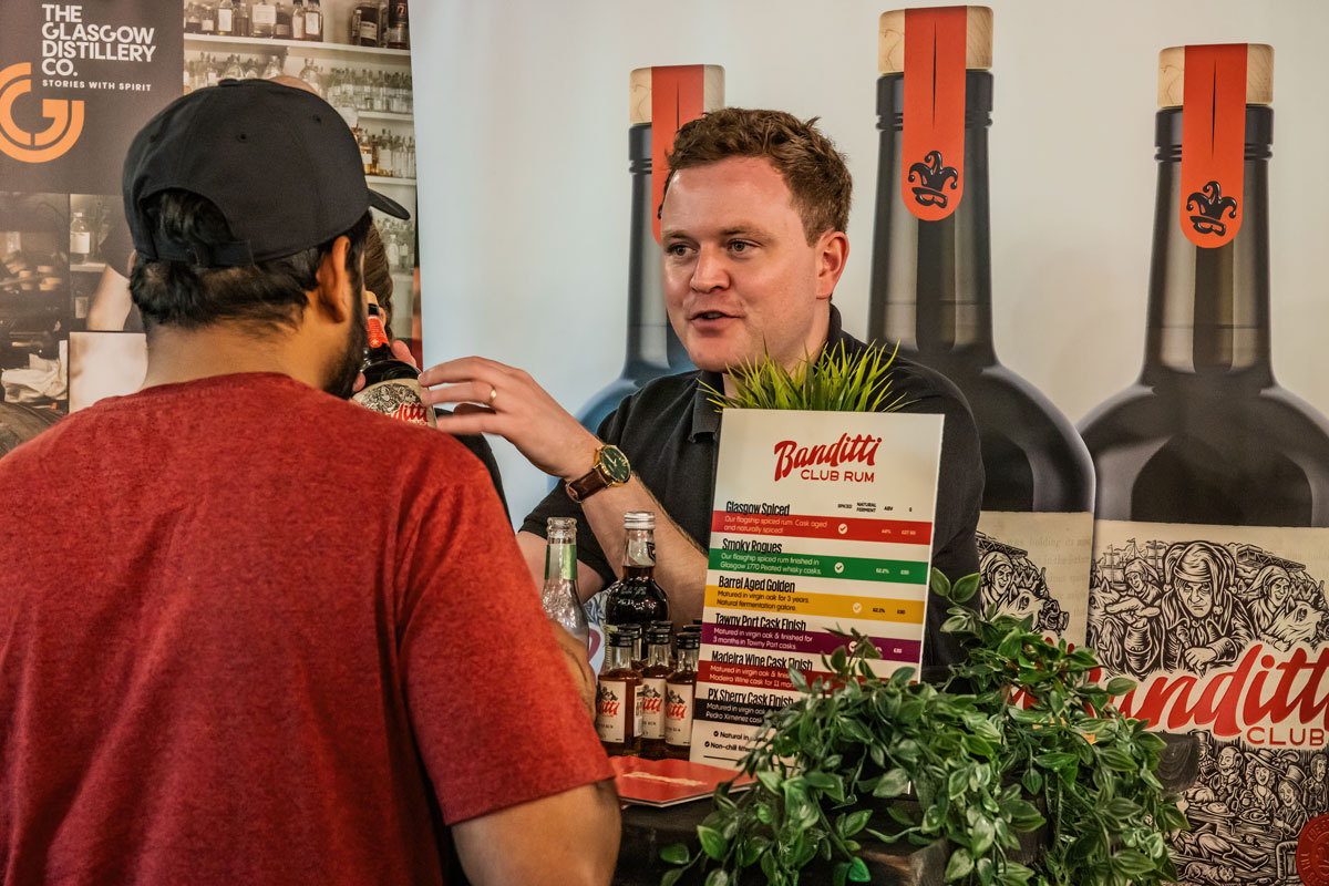 A man hands out drink samples from behind a table covered in bottles