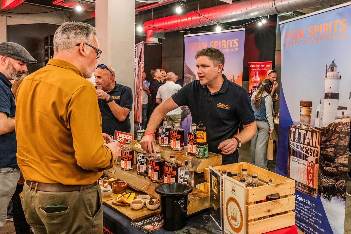 A man hands out drink samples from behind a table covered in bottles