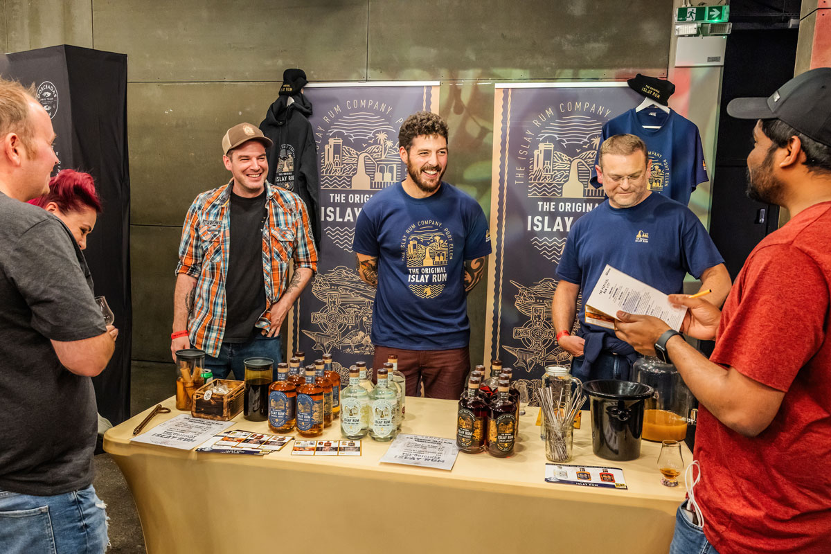 Three men stand behind a table covered in bottles