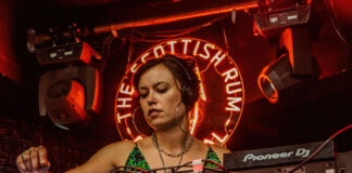A young woman DJs against a red neon background
