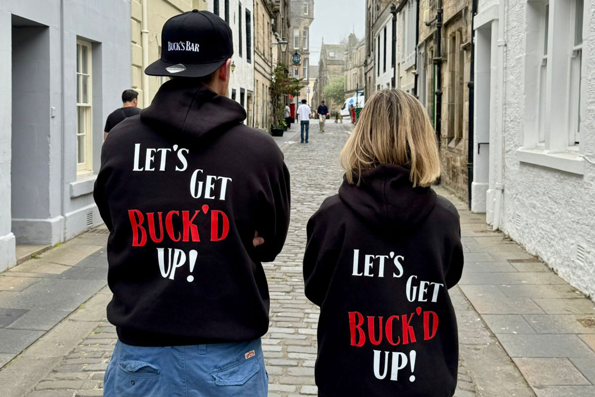 A man and a woman in slogan hoodies stand in an old fashion side street
