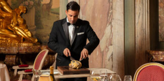 A smartly dressed waiter carves a chicken