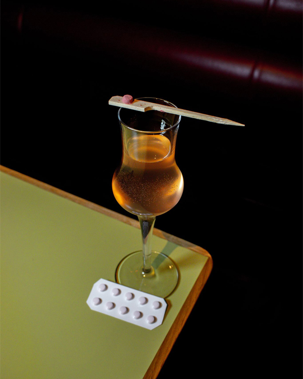 whisky cocktail with a pink pill balanced