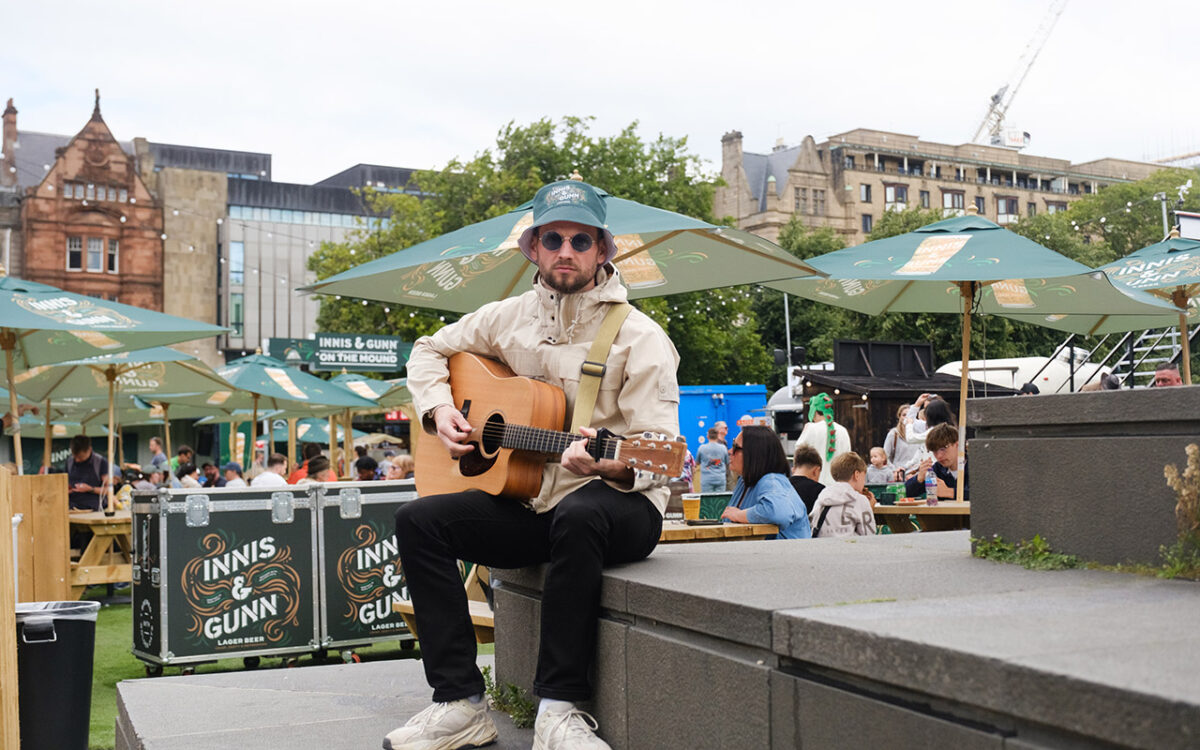 Man dressed in the style of Oasis sitting with a guitar.