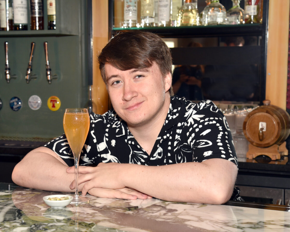 Bartender Ewan Robertson leaning on the bar with his cocktail.